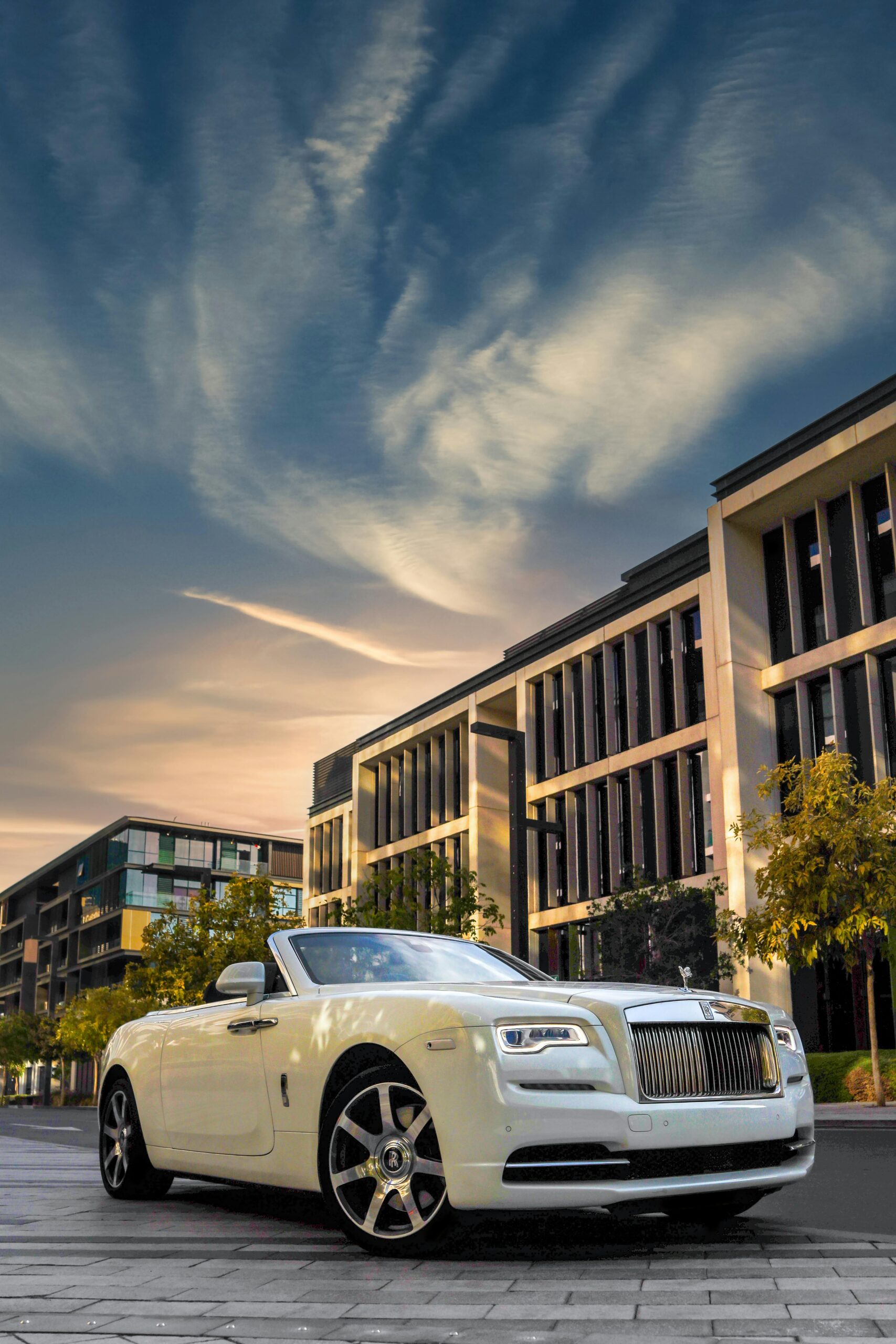 Elegant white Rolls Royce parked against Dubai's modern architectural skyline at dawn.